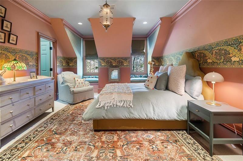 Another upstairs bedroom takes on a slightly bolder palette with muted pink walls, decorative wallpaper borders, and patterned rugs layered across the floors. 