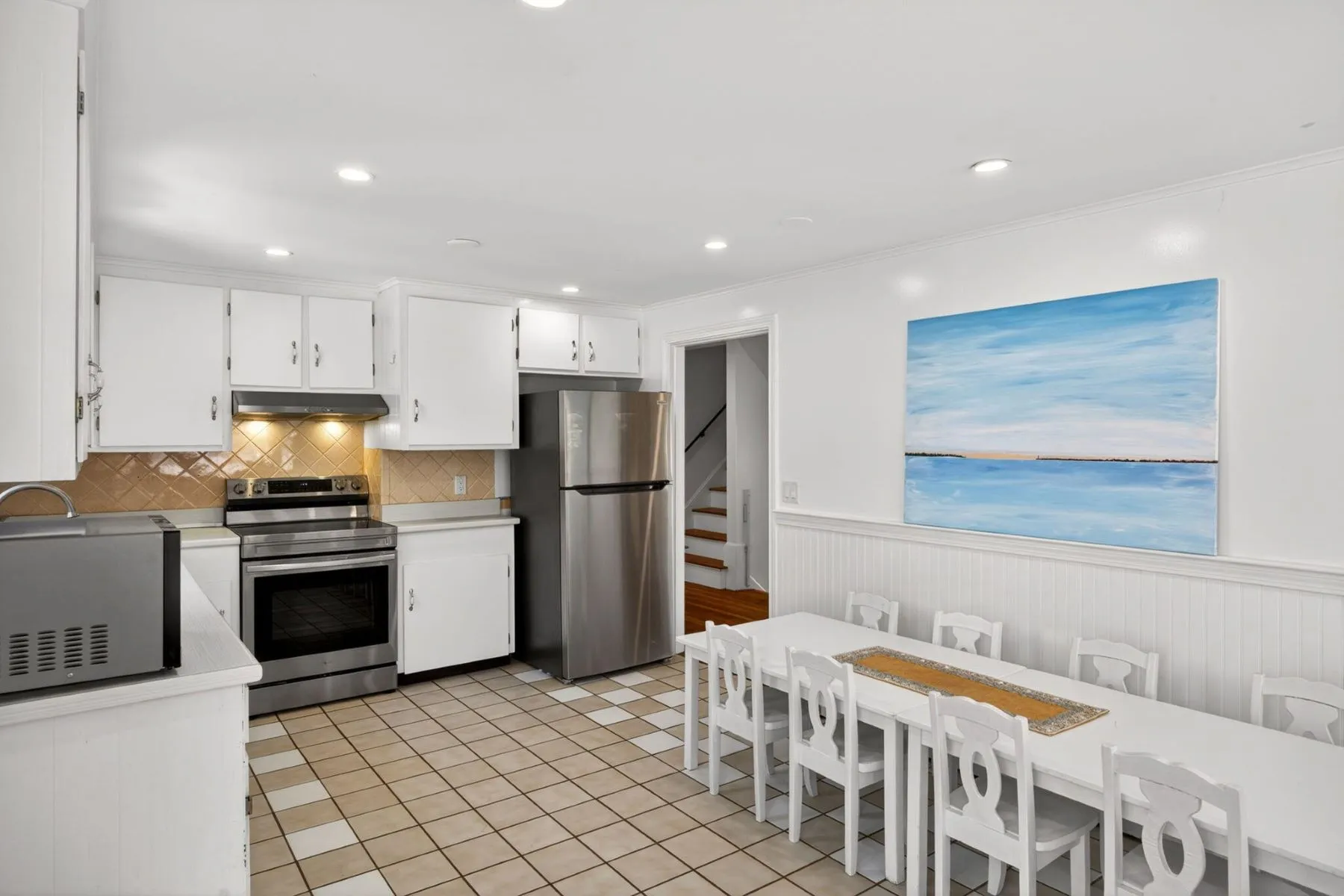 Within the same open area is the kitchen, a bright and highly functional space designed with white cabinetry, simple tile flooring, and stainless steel appliances.