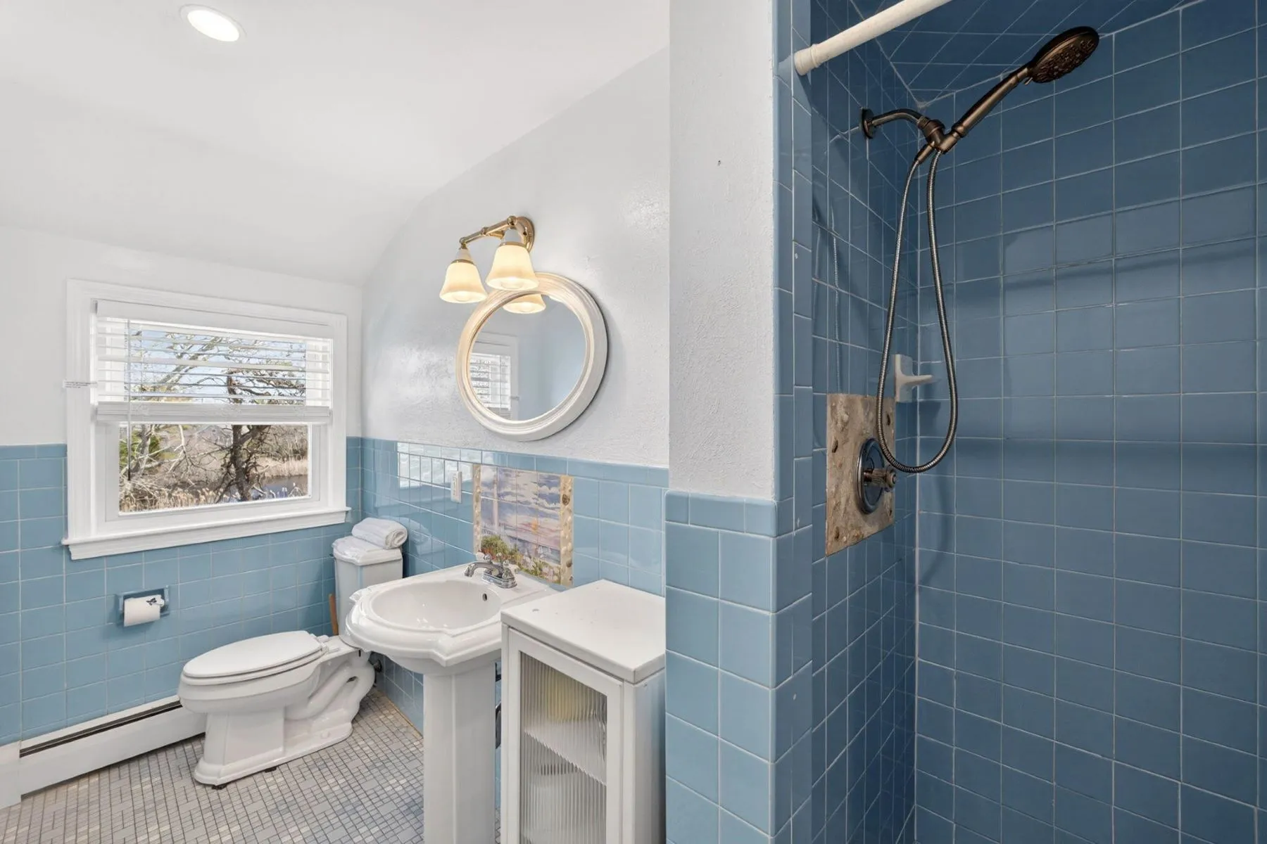 Another bathroom has a softer coastal palette with light blue tile wrapping around the shower and lower walls. 
