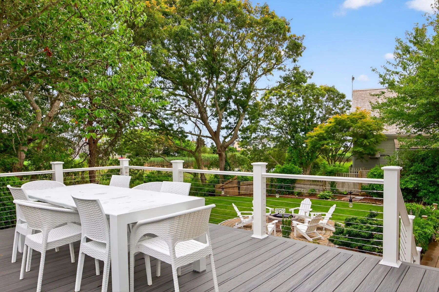 White railings and matching outdoor furniture keep the setup simple and coastal, while the elevated vantage point looks down over the landscaped backyard and nearby pond.