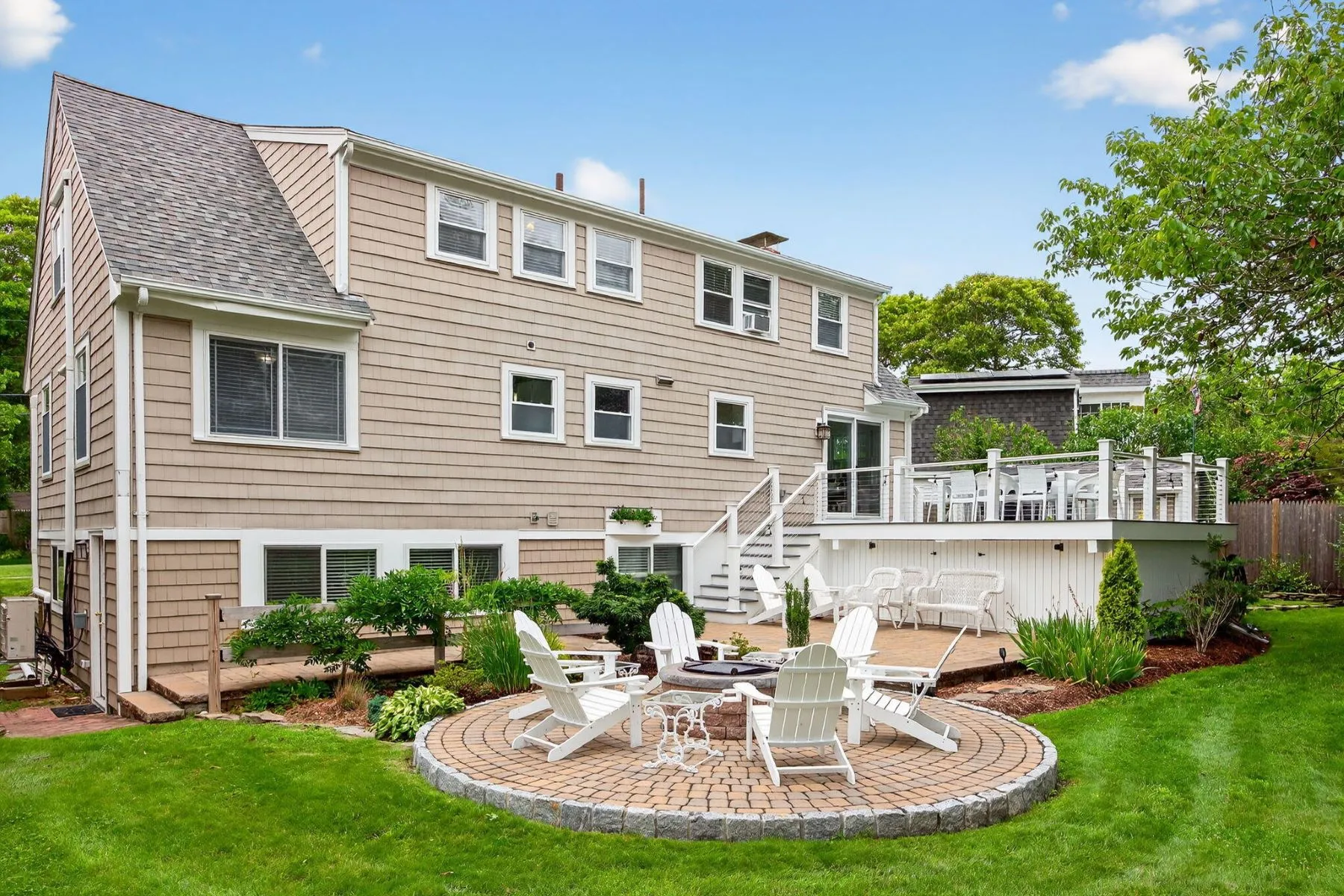 Below the deck, a circular brick patio centers around a fire pit surrounded by Adirondack chairs.