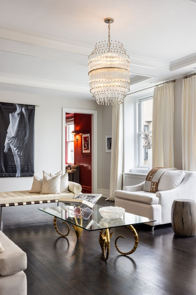 Soft gray walls and layered white trim are complemented by a tiered crystal chandelier that hangs over the center seating arrangement.