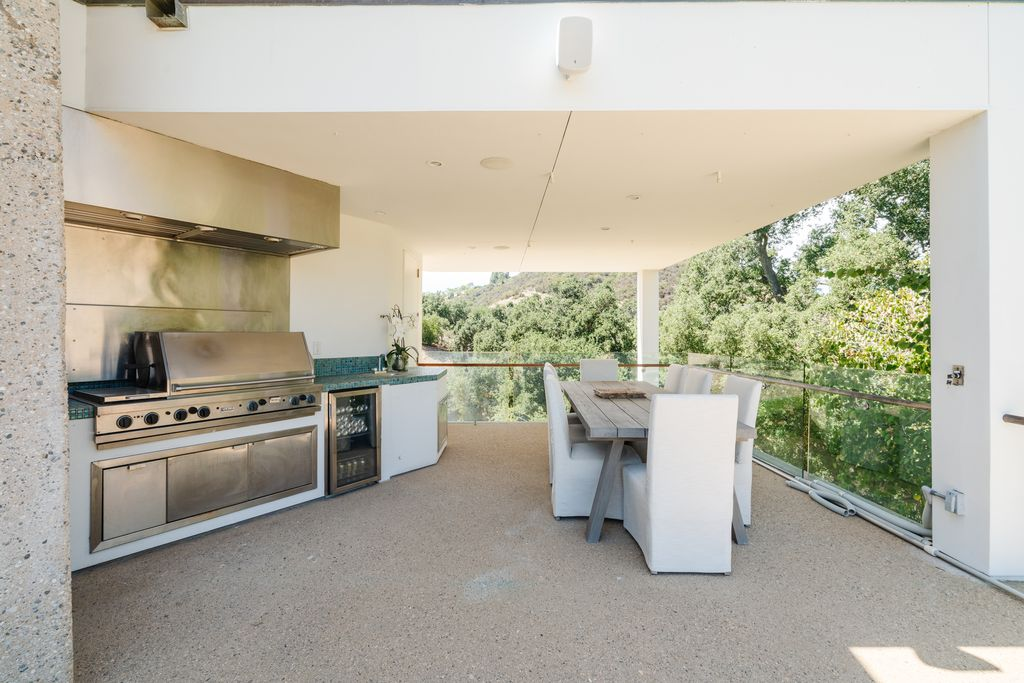 As the patio curves around the side of the house, it transitions into a covered outdoor kitchen tucked beneath a shaded terrace overlooking the hillsides. 