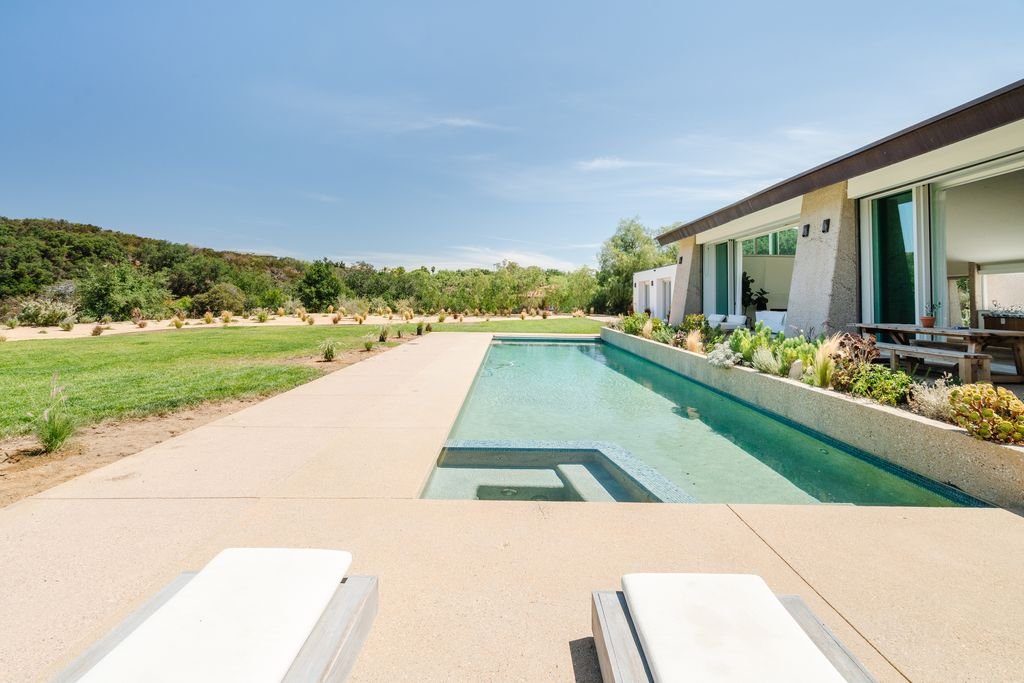 A few steps below, the backyard opens into the pool terrace, where the long rectangular pool runs parallel to the house and reflects the clean horizontal lines of the architecture. 