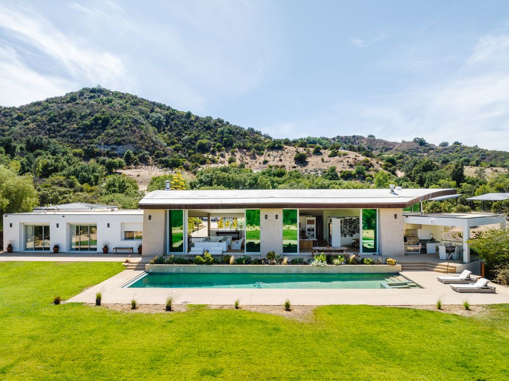 Wide concrete decking surrounds the water, leaving large expanses of open lawn beyond the pool and creating uninterrupted sightlines toward the rolling Topanga hills. 