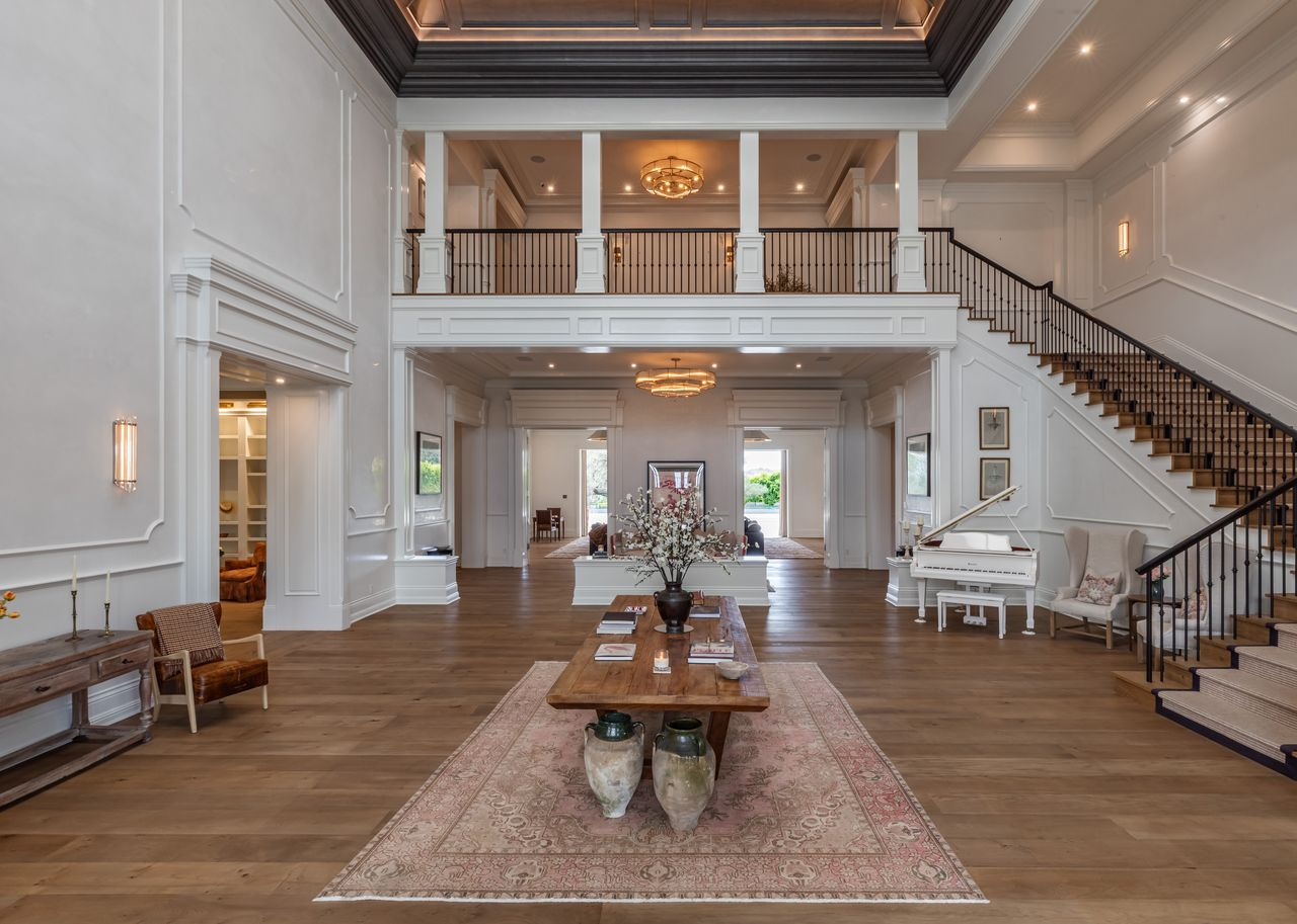 Soaring skylit ceilings rise above the two-story space, drawing natural light down across the paneled walls and wide-plank wood floors, while a dark coffered ceiling detail adds contrast overhead.