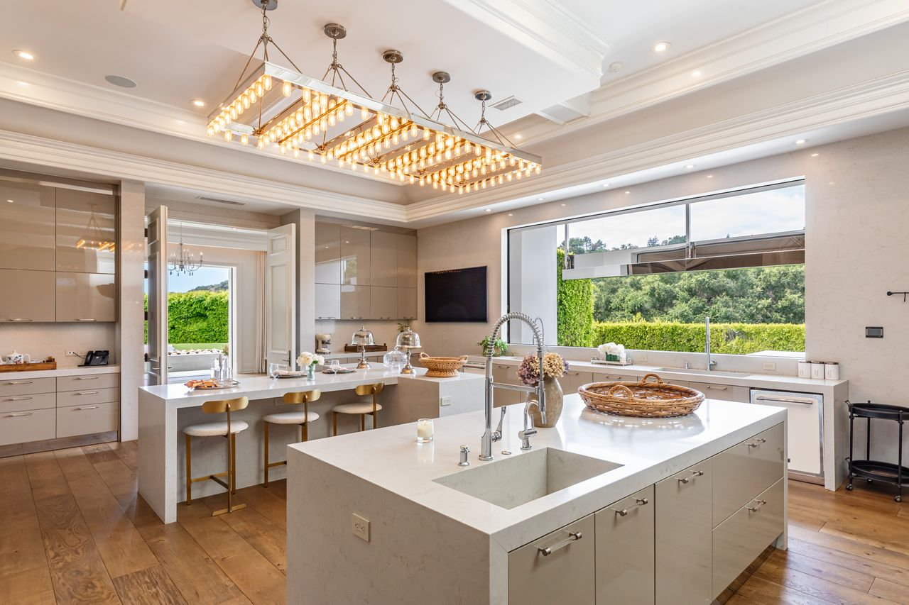 Glossy cabinetry stretches wall to wall, while wide windows above the sink bring in views of the greenery outside and pull natural light across the stone surfaces.