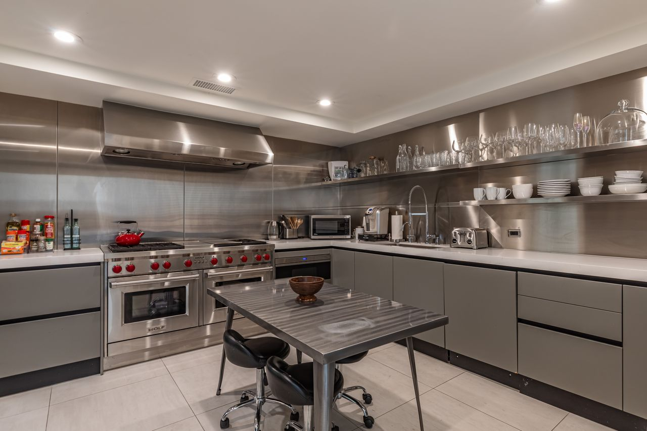 To support larger-scale cooking, the secondary kitchen sits just around the corner with stainless steel walls, open shelving, industrial-grade ventilation, and a Wolf range. 