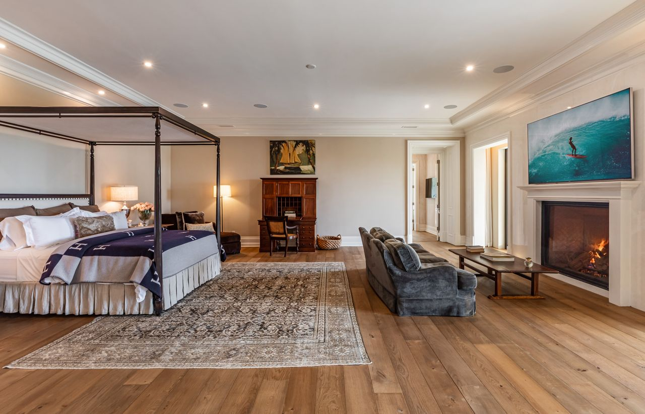 The bedroom centers around a dark metal canopy bed positioned beside a fireplace seating area, creating two distinct zones within the same open space.