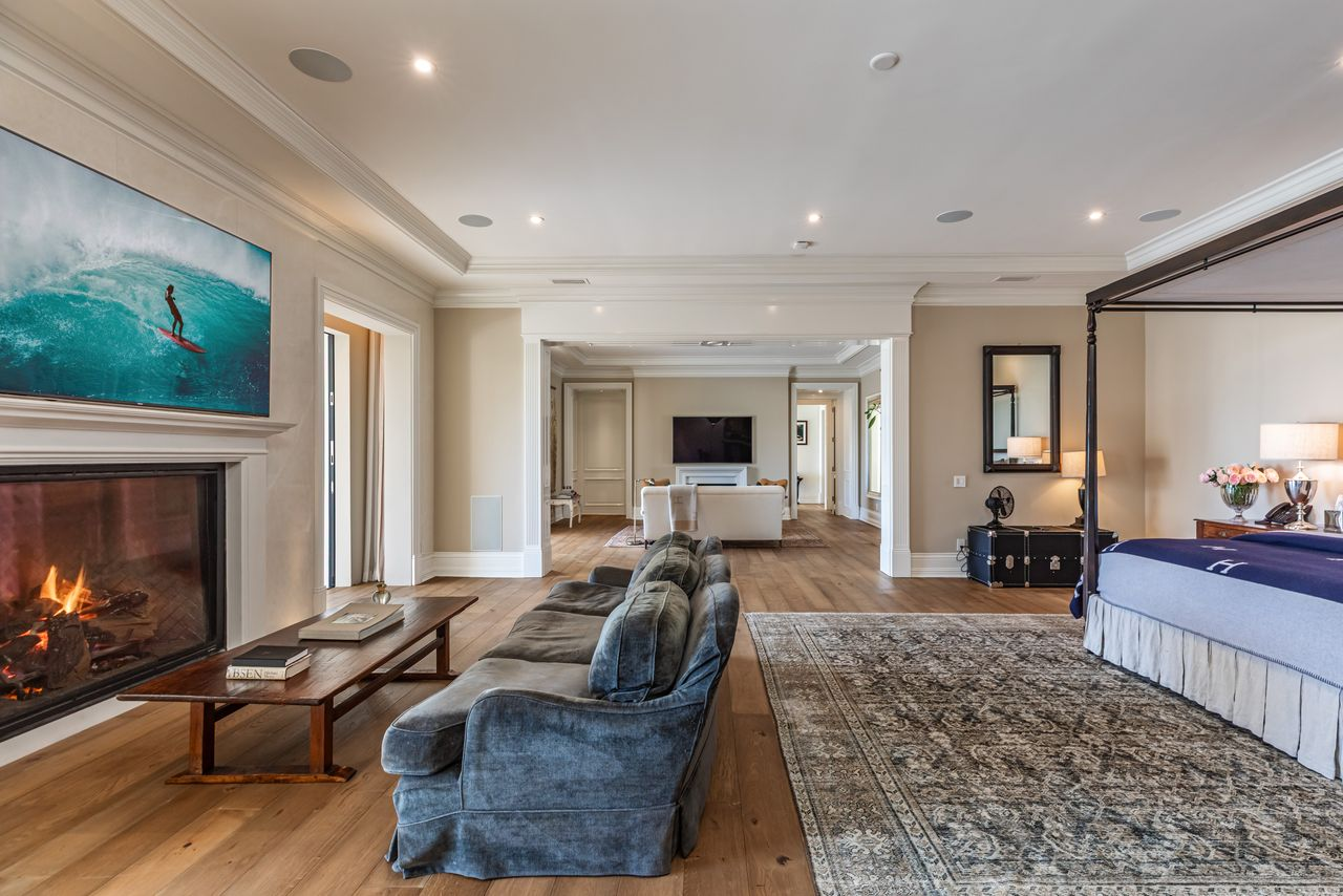 A sitting area with a low velvet sofa faces the fireplace, turning one side of the suite into a dedicated lounge separate from the sleeping area. 