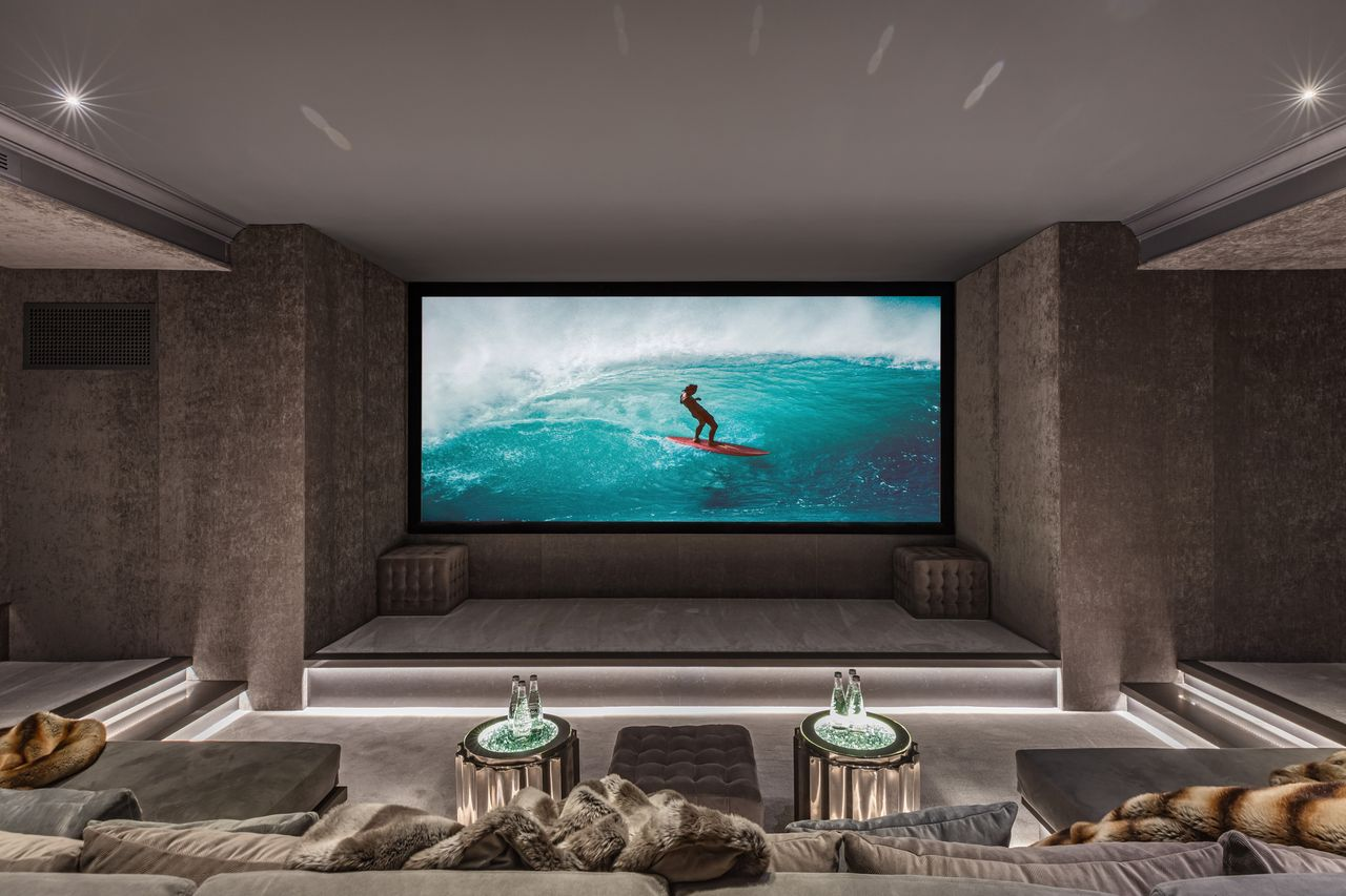 The theater introduces a dramatically darker palette, wrapped in textured wall coverings and soft integrated lighting that directs attention toward the oversized projection screen. 