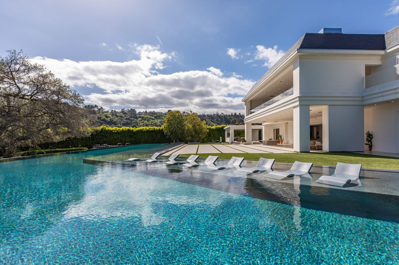 The zero-edge pool stretches across the width of the backyard with a shallow lounging shelf lined with in-water chaise chairs along one side. 