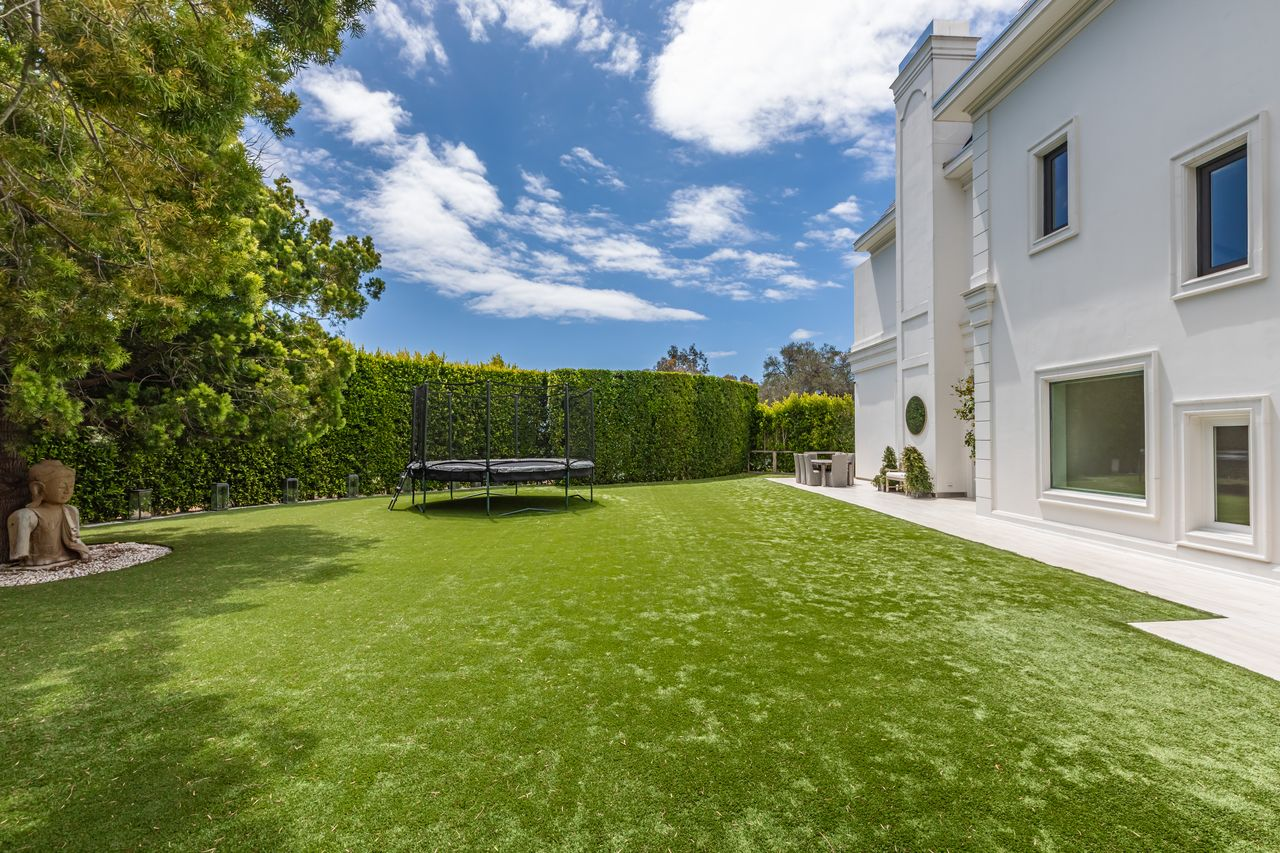 Beyond the pool deck, the property opens into broad grassy lawns bordered by mature hedges and trees that create privacy around the estate.