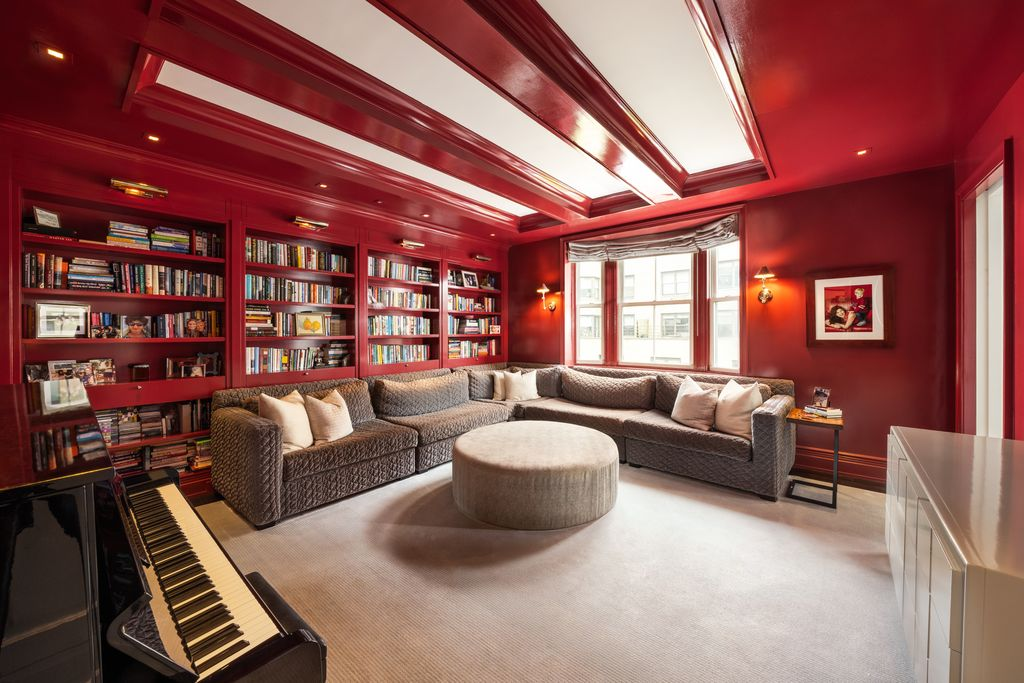 The entire room is wrapped in deep lacquered red, from the walls and built-in bookshelves to the ceiling trim, creating a dramatic contrast against the lighter palette of the surrounding entertaining spaces.