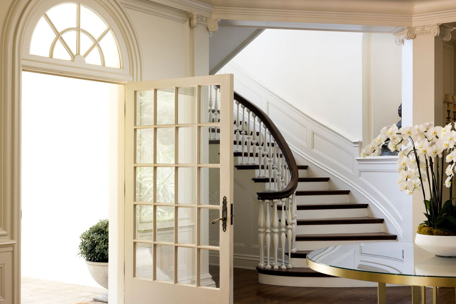 French-pane doors swing open beneath detailed crown molding and decorative columns, while the dark wood stair treads contrast against the bright white paneling and walls, reinforcing the home’s early 20th-century roots.
