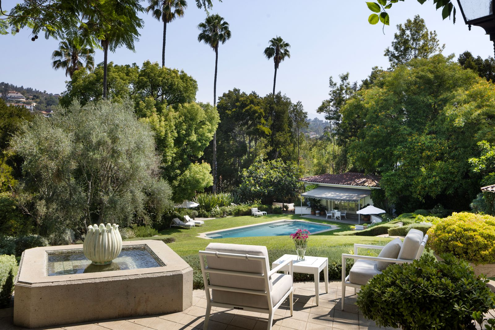 At this particular spot, a small fountain sits beside an outdoor lounge overlooking the lawn and pool pavilion, adding another quiet perch designed for outdoor living at the historic compound.