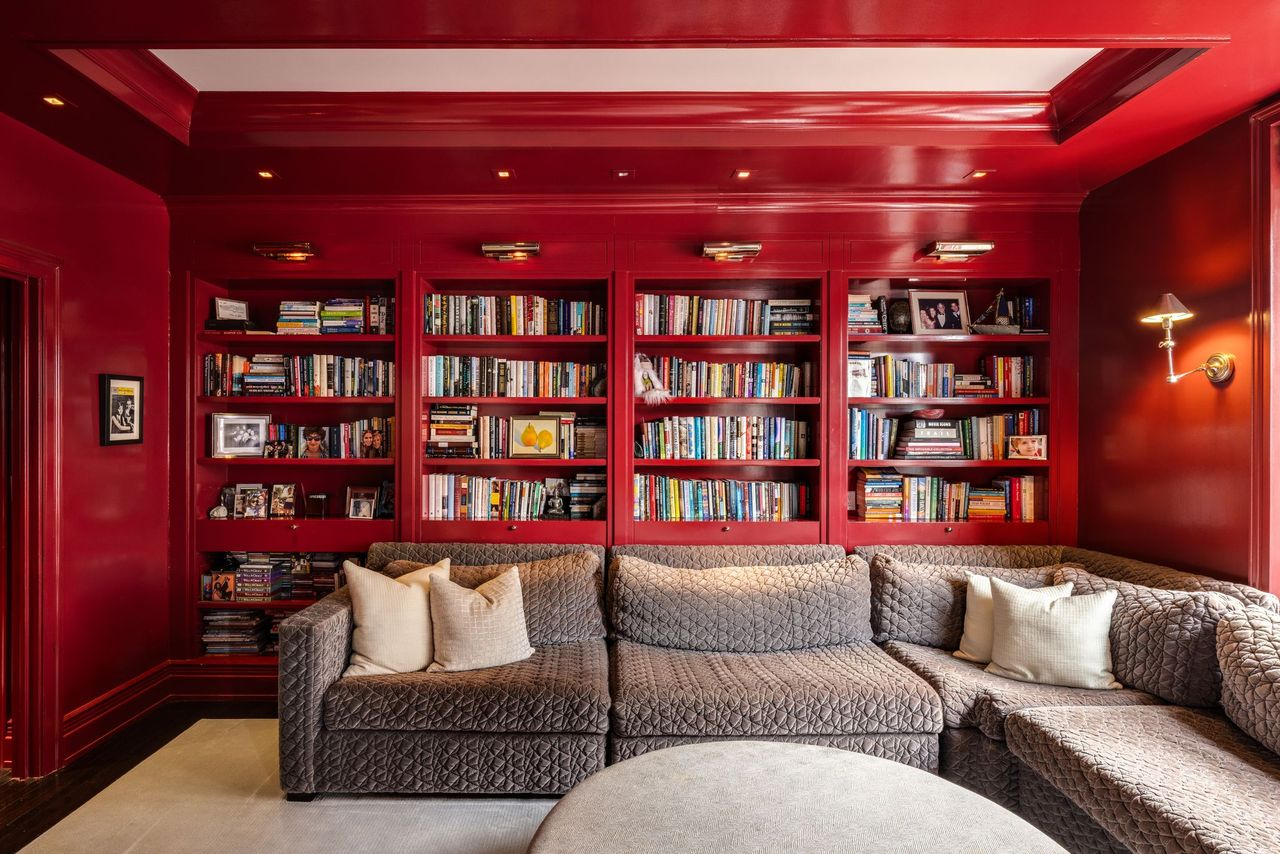 Floor-to-ceiling shelving lines one wall, filled with books, framed photographs, and personal mementos, while a large sectional sits directly in front of it.