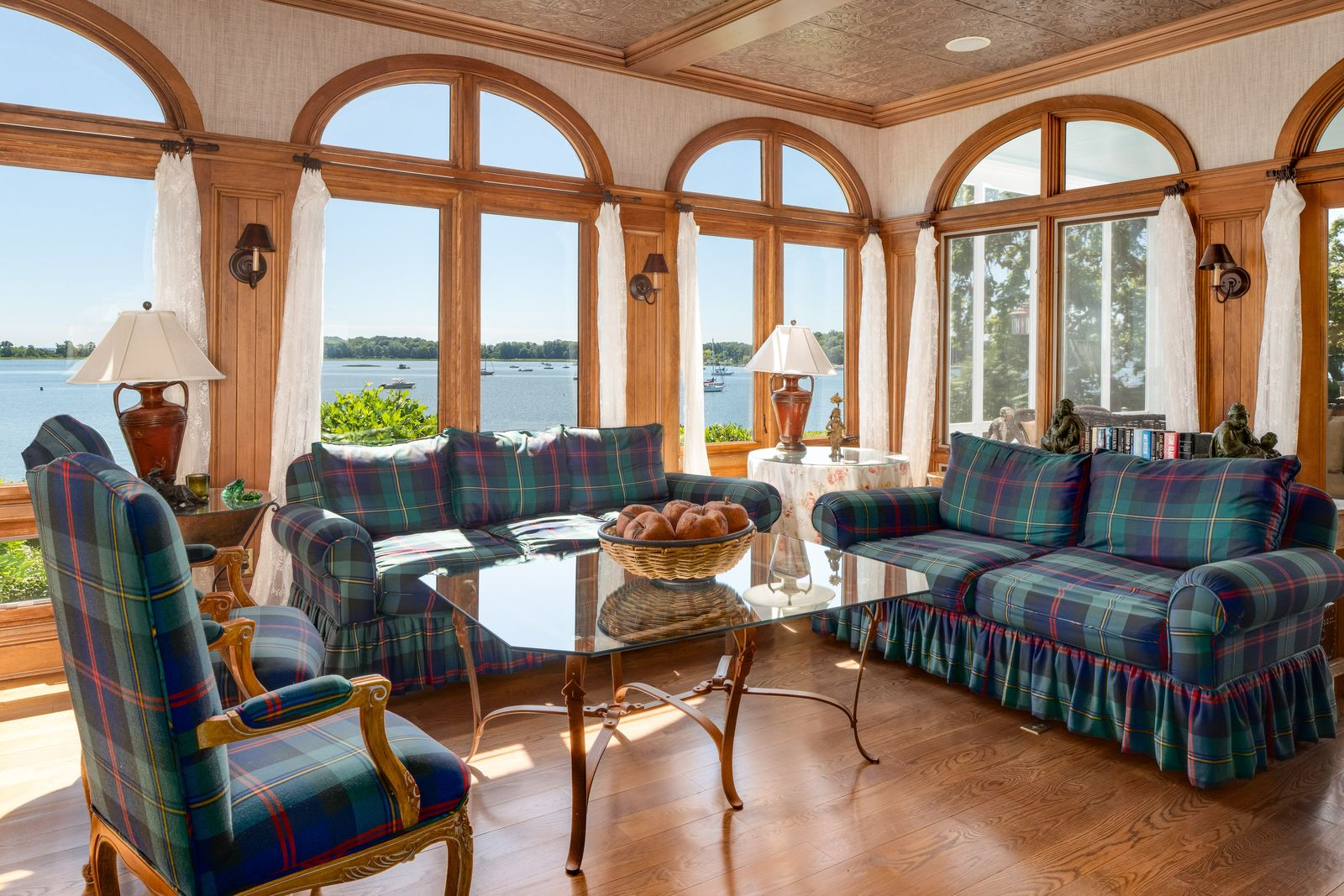 Walls of arched windows frame wide water views while bringing natural light across the antique wood floors, highlighting the detailed millwork and soaring ceilings that continue throughout the residence.