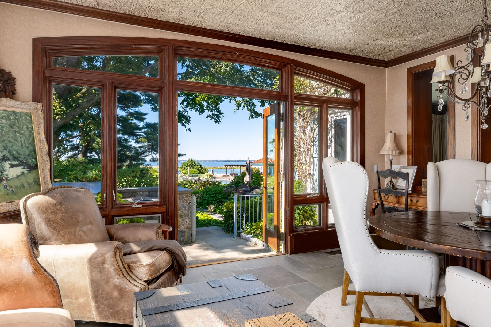 A mix of leather seating, antique furnishings, and a round wood table creates a setting designed for reading, conversation, or quieter gatherings with direct access to the gardens outside.