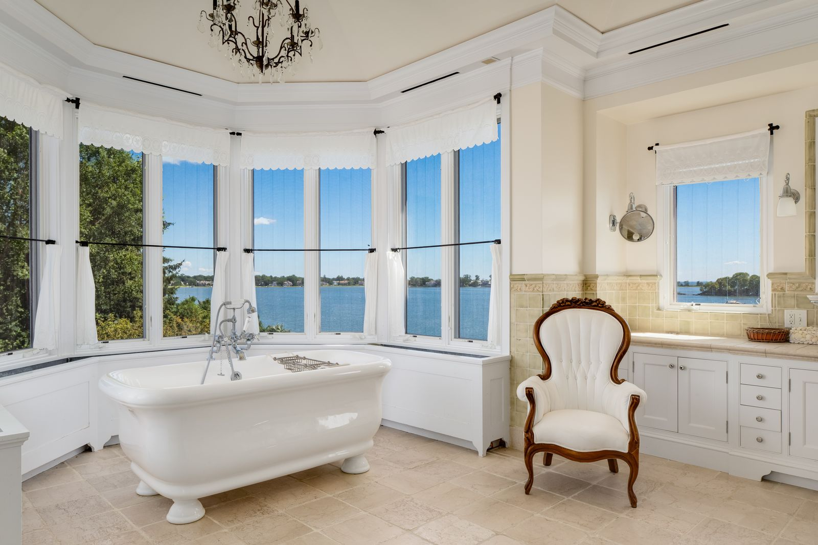 Inside the primary bathroom, a freestanding soaking tub is positioned in front of a curved wall of windows overlooking the water. 