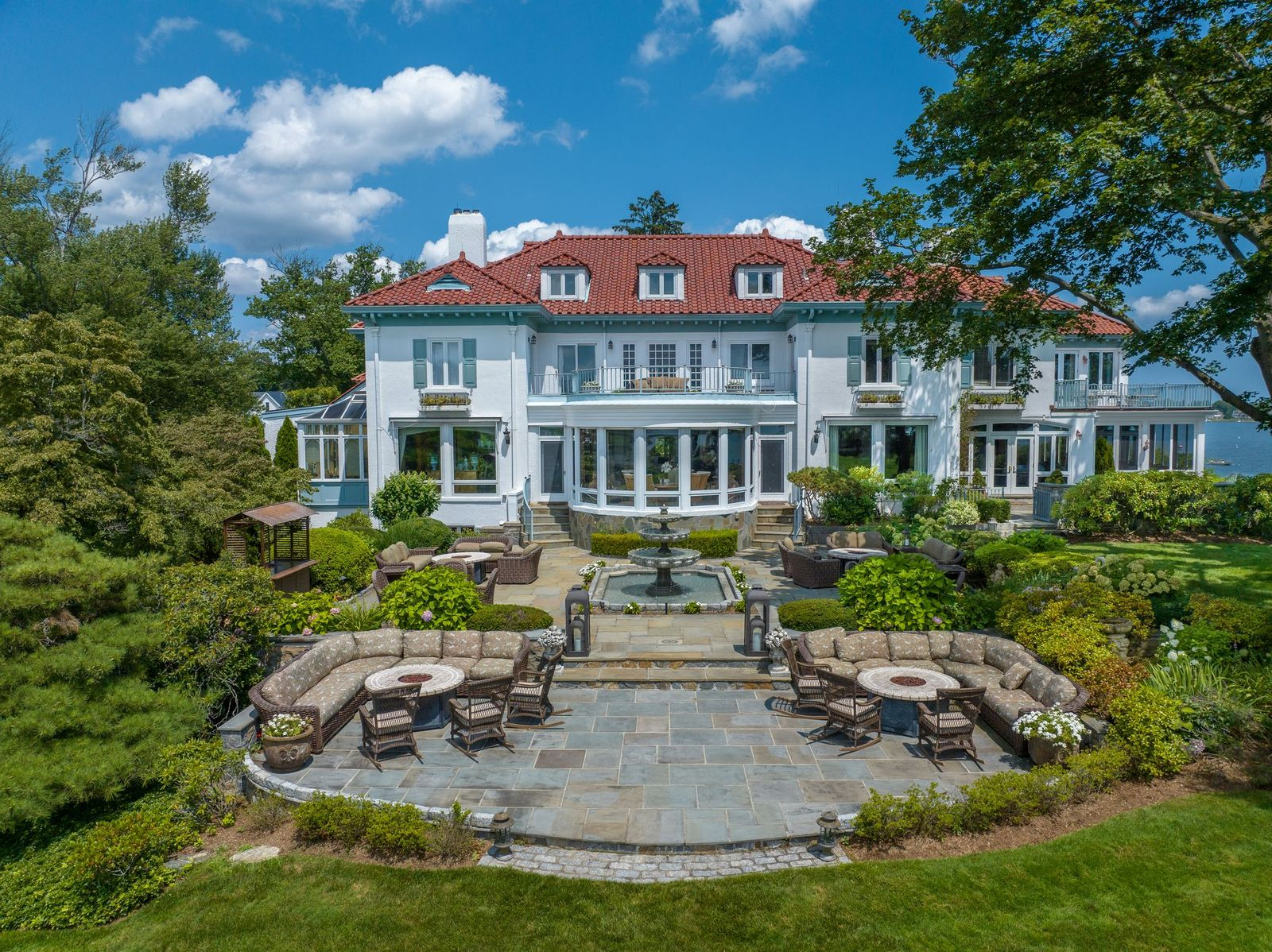 Directly behind the home, a large stone patio begins the grounds with multiple curved seating areas arranged around a tiered fountain. 