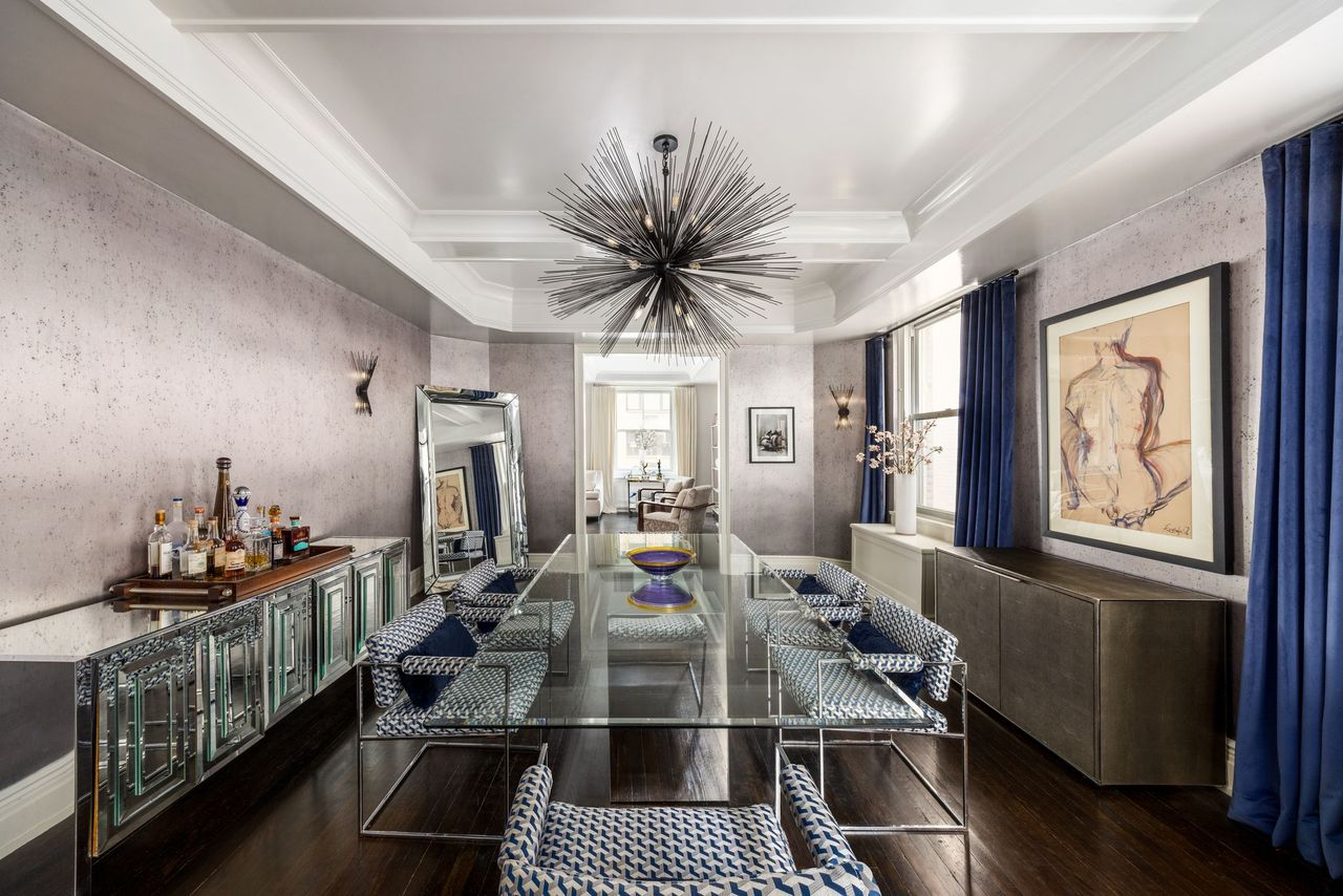 Inside, a long glass dining table runs through the center of the room beneath a sculptural black chandelier, with patterned upholstered chairs arranged along either side.