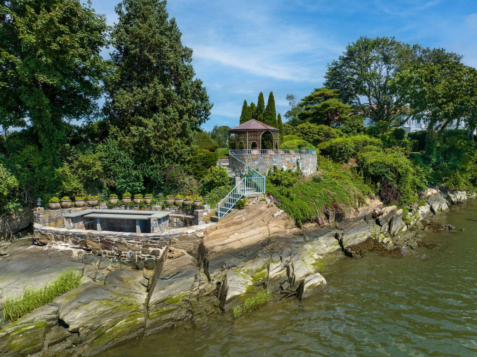 Stone retaining walls and steps connect a raised gazebo perched above the water and a lower bar, creating a tucked-away area for outdoor entertaining.