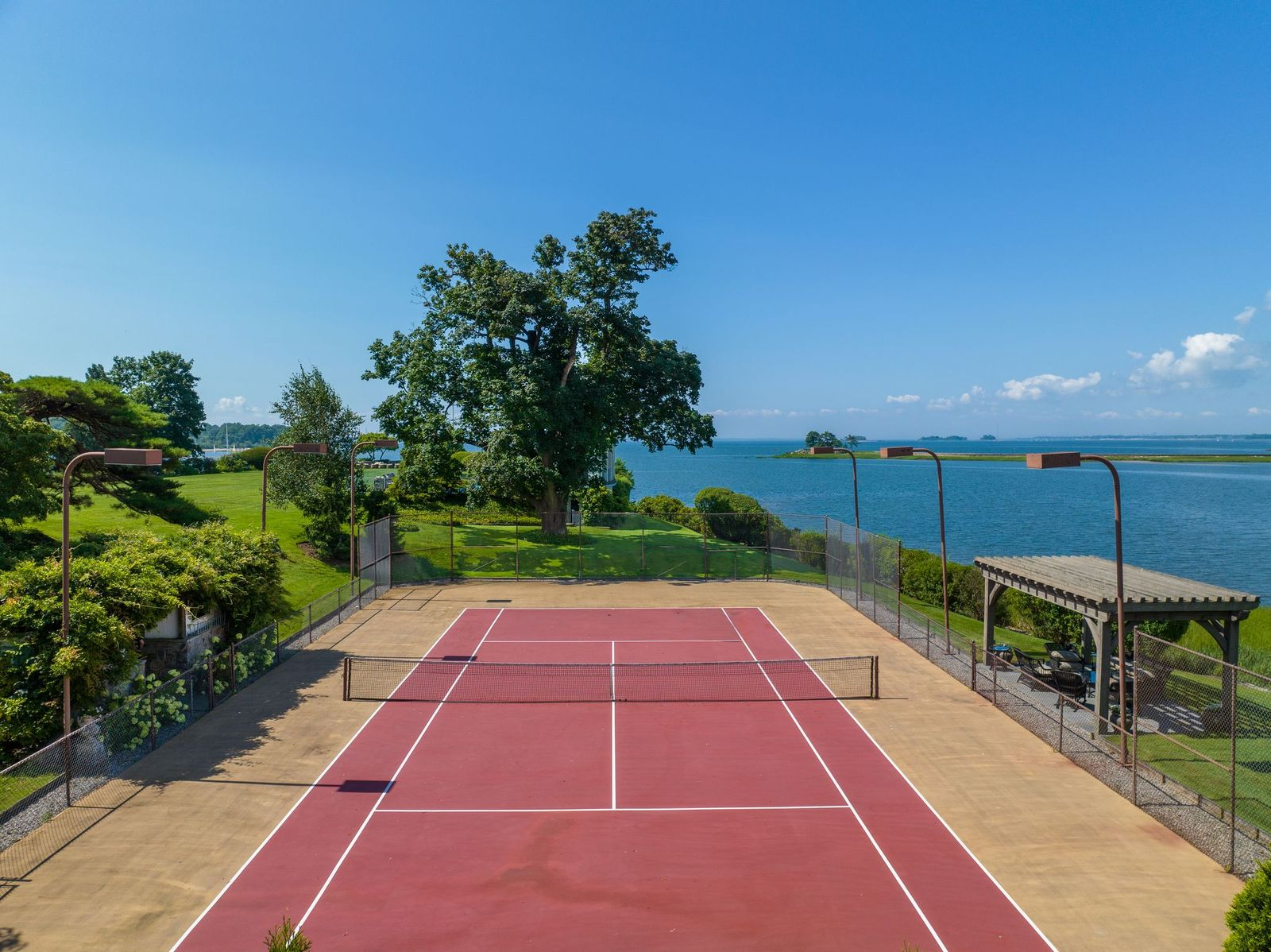 The full-size tennis court sits along the edge of the property with panoramic views extending across the water. 