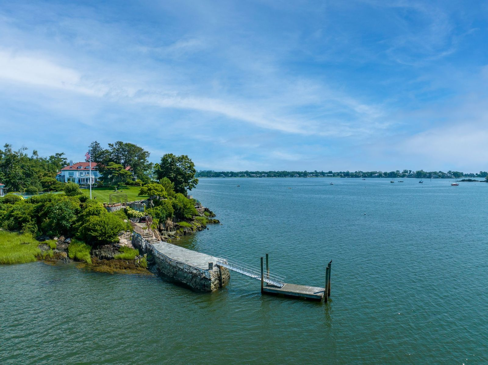At the shoreline, a substantial stone pier extends outward into the bay, connecting to a private deep-water dock capable of accommodating larger vessels. 