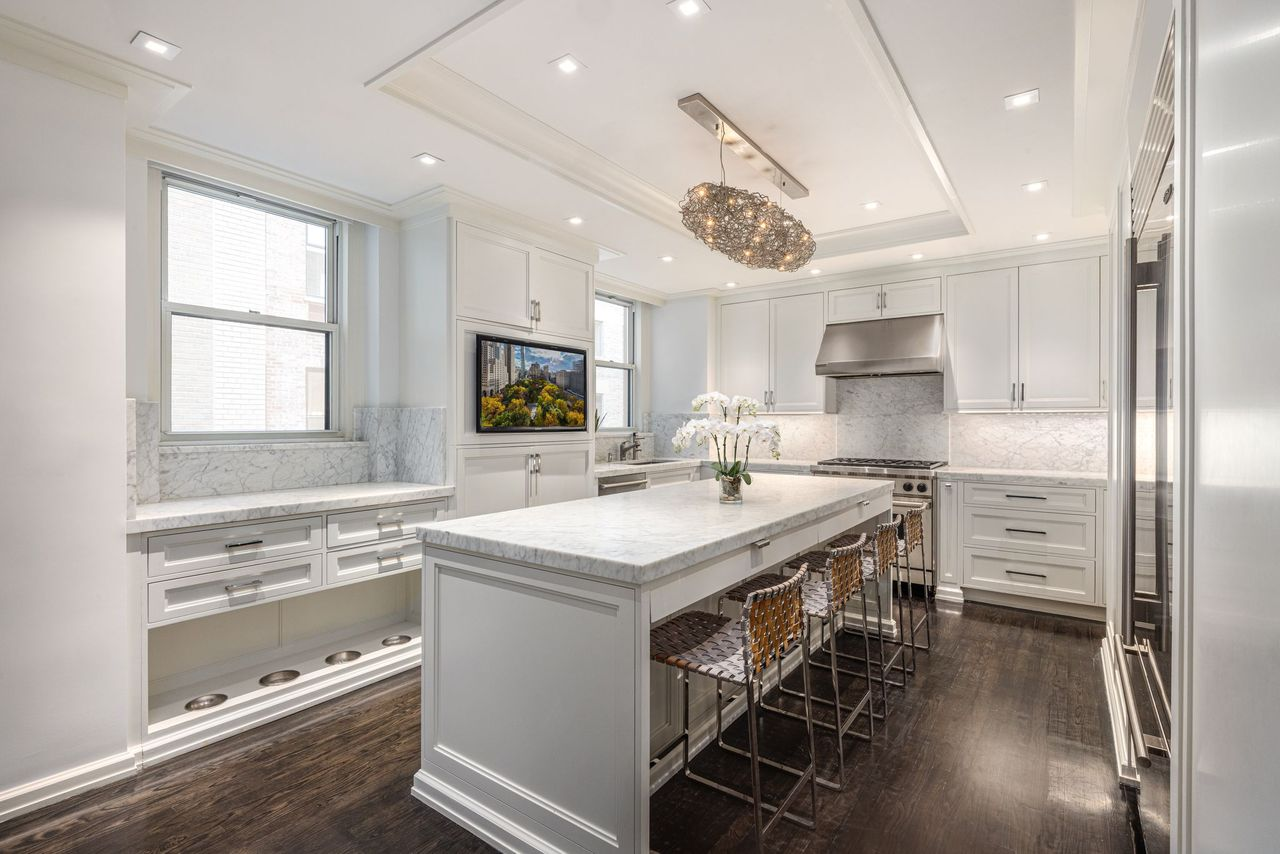 The kitchen shifts into a brighter, more streamlined design centered around Carrara marble countertops and custom white cabinetry. 