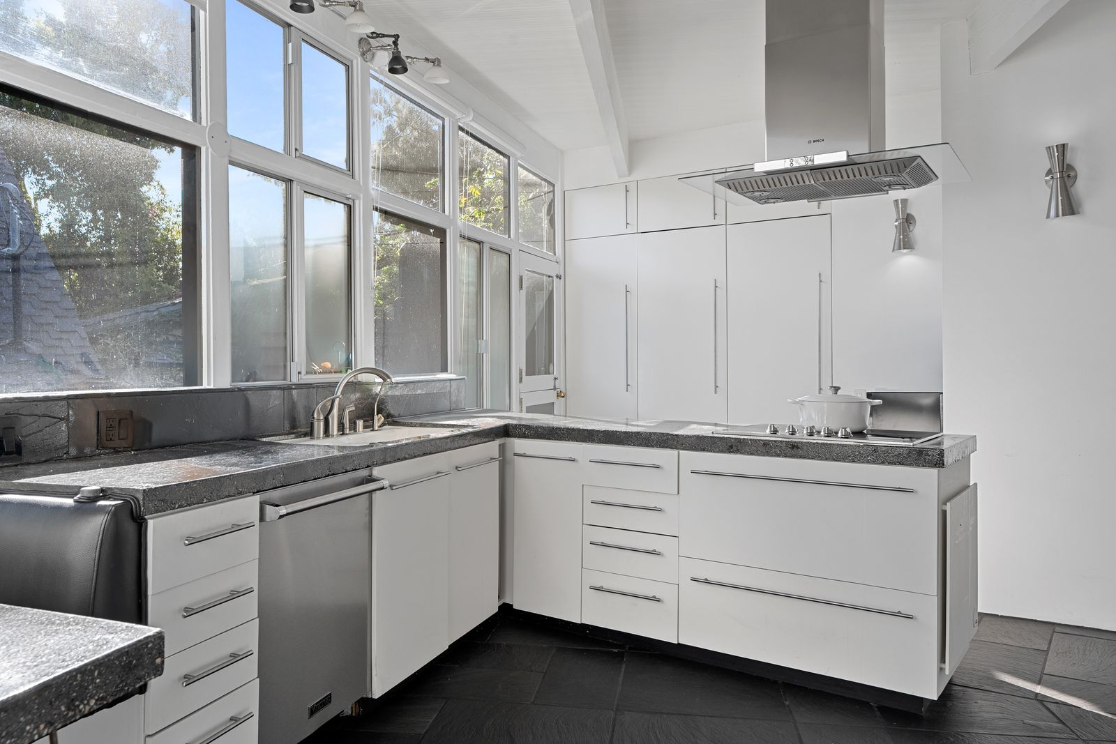 Towards the back, white flat-panel cabinetry stretches from floor to ceiling, while dark stone countertops and slate flooring create contrast against the bright palette.