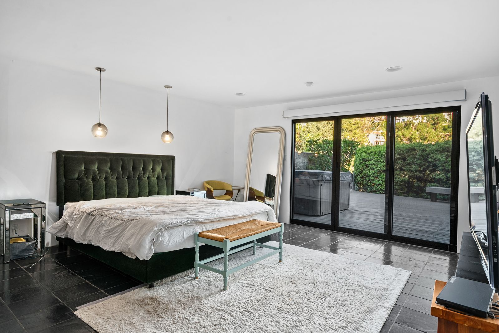 The bedroom itself has a minimalist layout, centered around a dark upholstered bed beneath suspended globe pendant lights. 