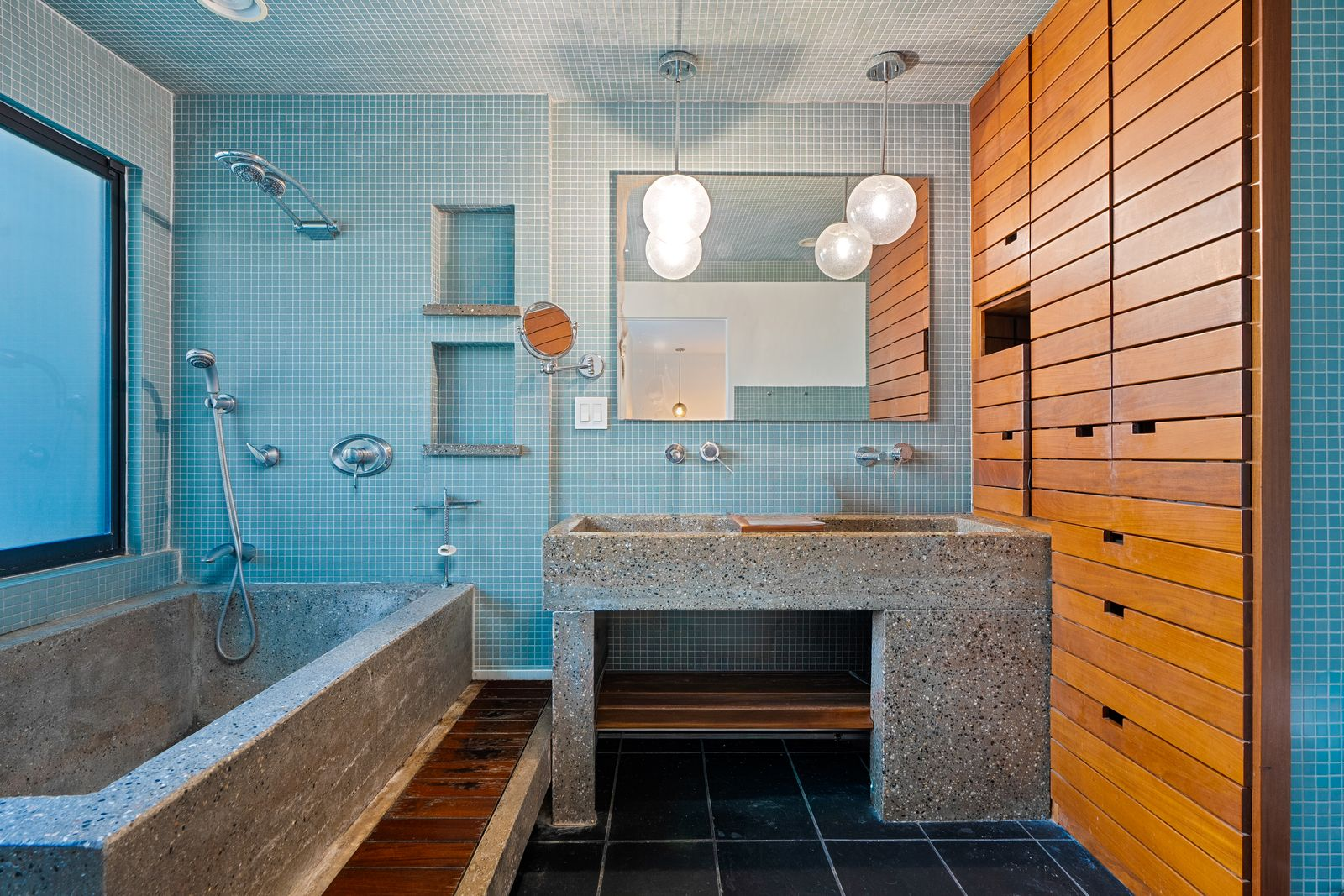 A deep soaking tub is built directly into the left corner beneath frosted windows, while the floating concrete vanity and integrated shelving maintain the room’s streamlined aesthetic in the middle.