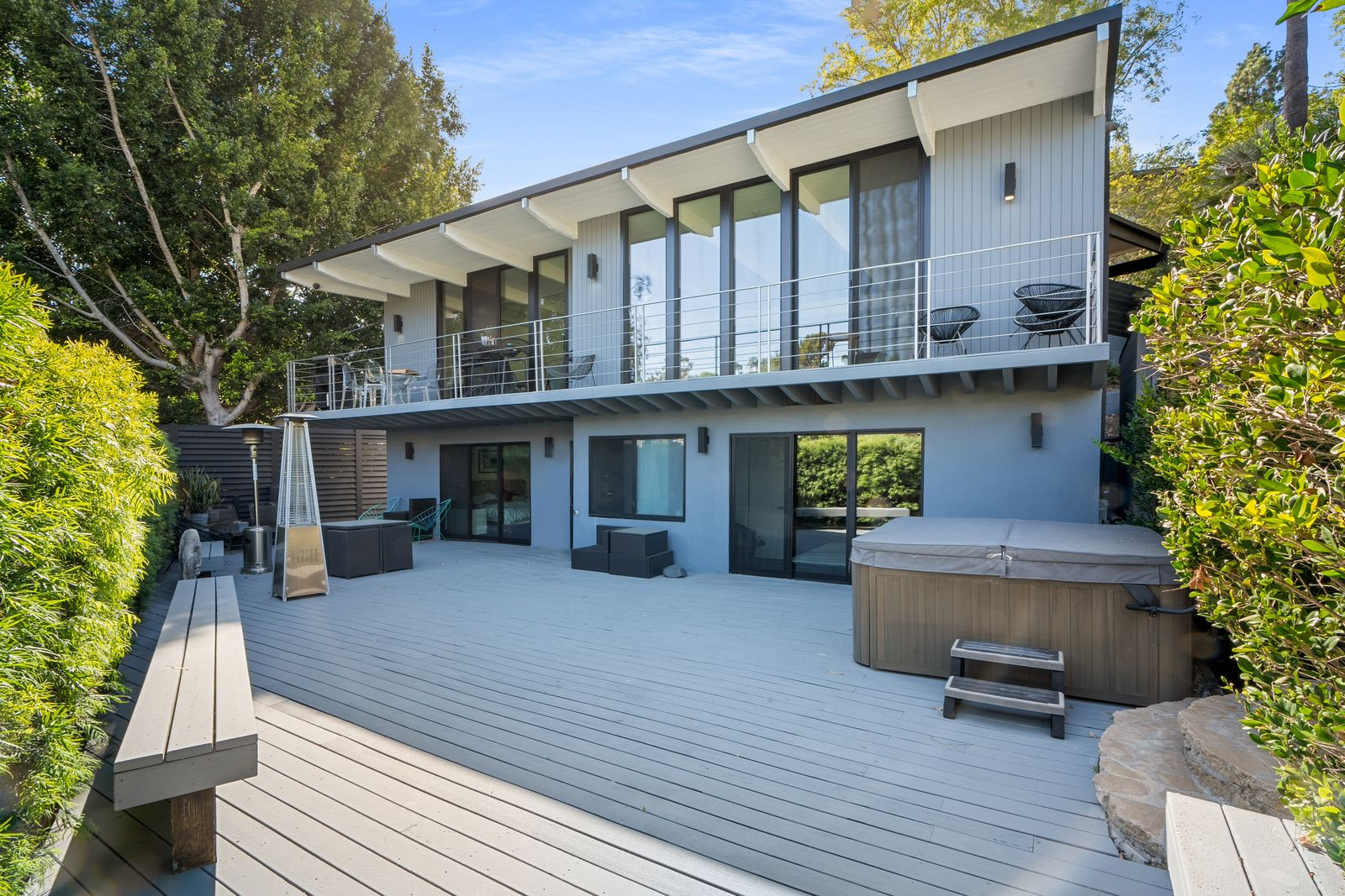 Sliding glass doors connect the space directly to the lower-level rooms, while outdoor seating areas, patio heaters, and a built-in hot tub turn the deck into a functional extension of the home.