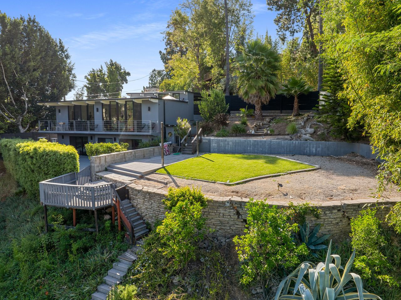 From there, the property steps outward into a layered backyard with retaining walls, elevated lawn sections, and multiple staircases woven into the hillside.