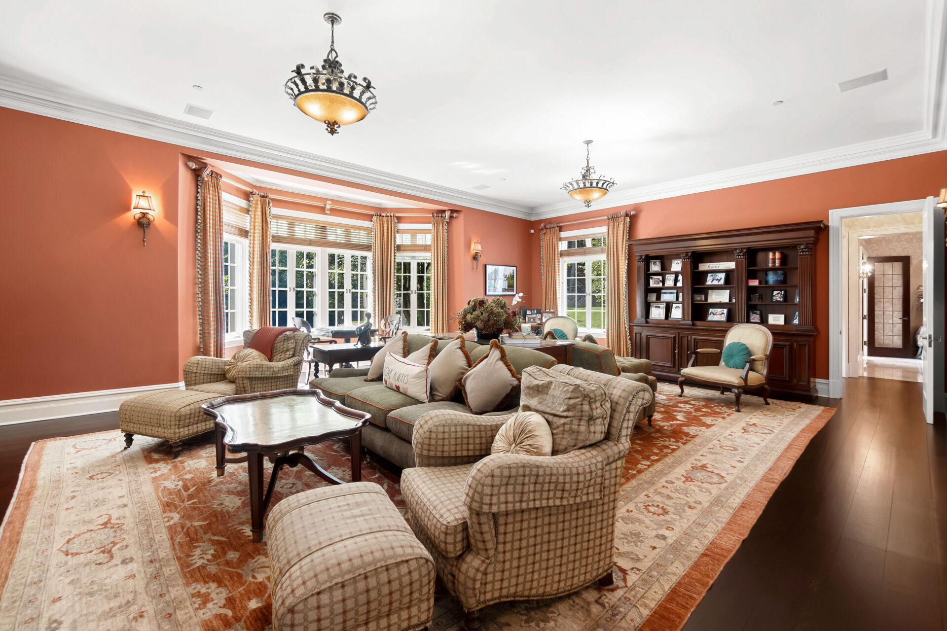 Rich terracotta-colored walls, dark hardwood floors, and layered traditional furnishings create a contrast to the bright marble finishes of the entry hall.