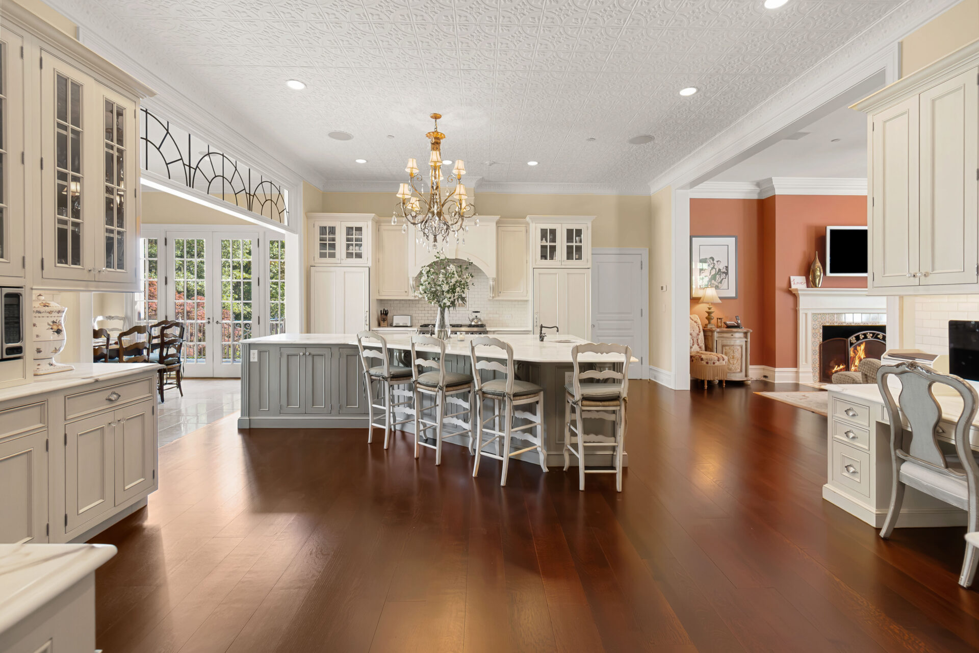 Kitchen with traditional design with custom cream-colored cabinetry, a decorative pressed-tin ceiling, and a large center island beneath a crystal chandelier.