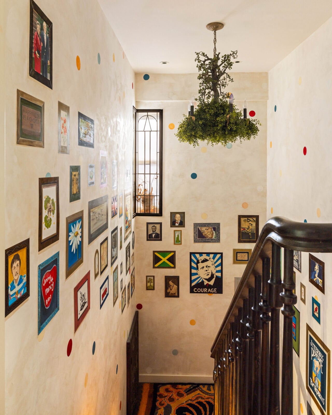 Stairwell with painted portraits lining the walls beneath a lush tree branch chandelier.