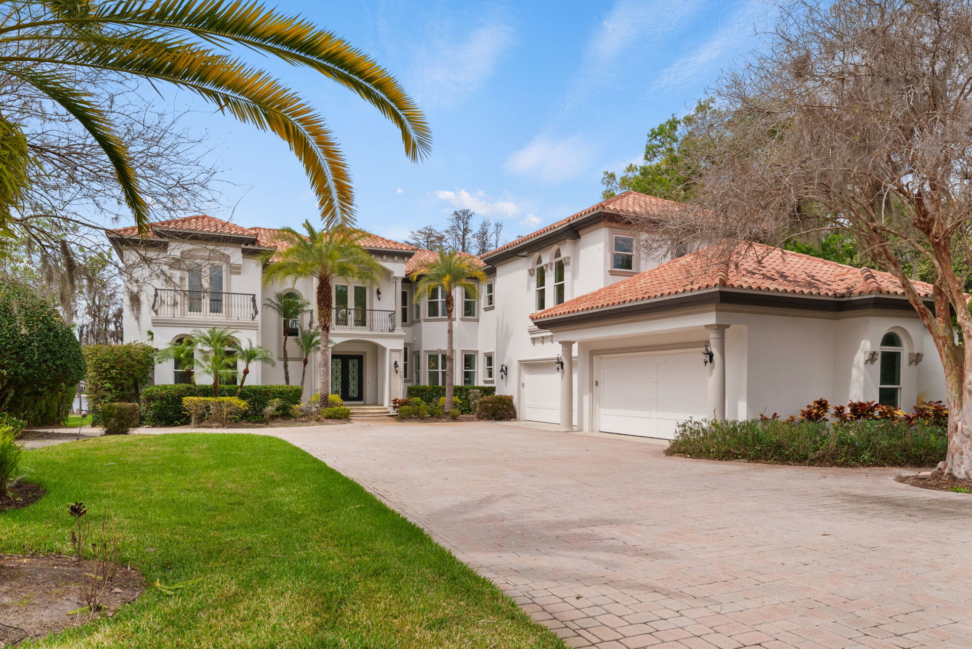 At the end of the drive, a broad motor court opens in front of the home, where stucco walls, arched windows, a terracotta tile roof, and a porte-cochère-style entry welcome you in.