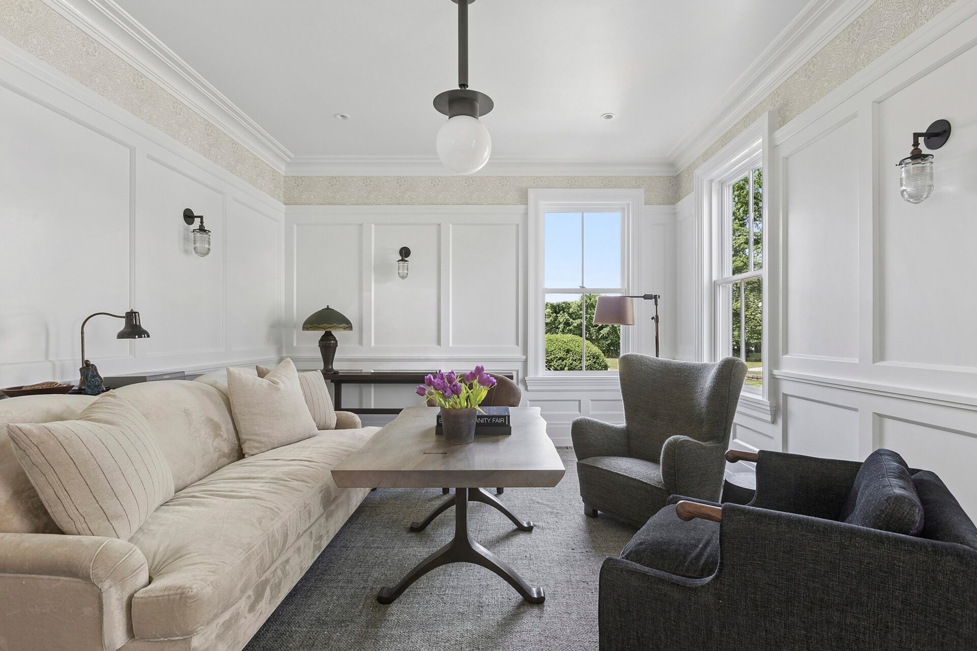 One lounge is arranged as an intimate sitting room, where a sofa and upholstered chairs surround a central table atop a textured area rug.