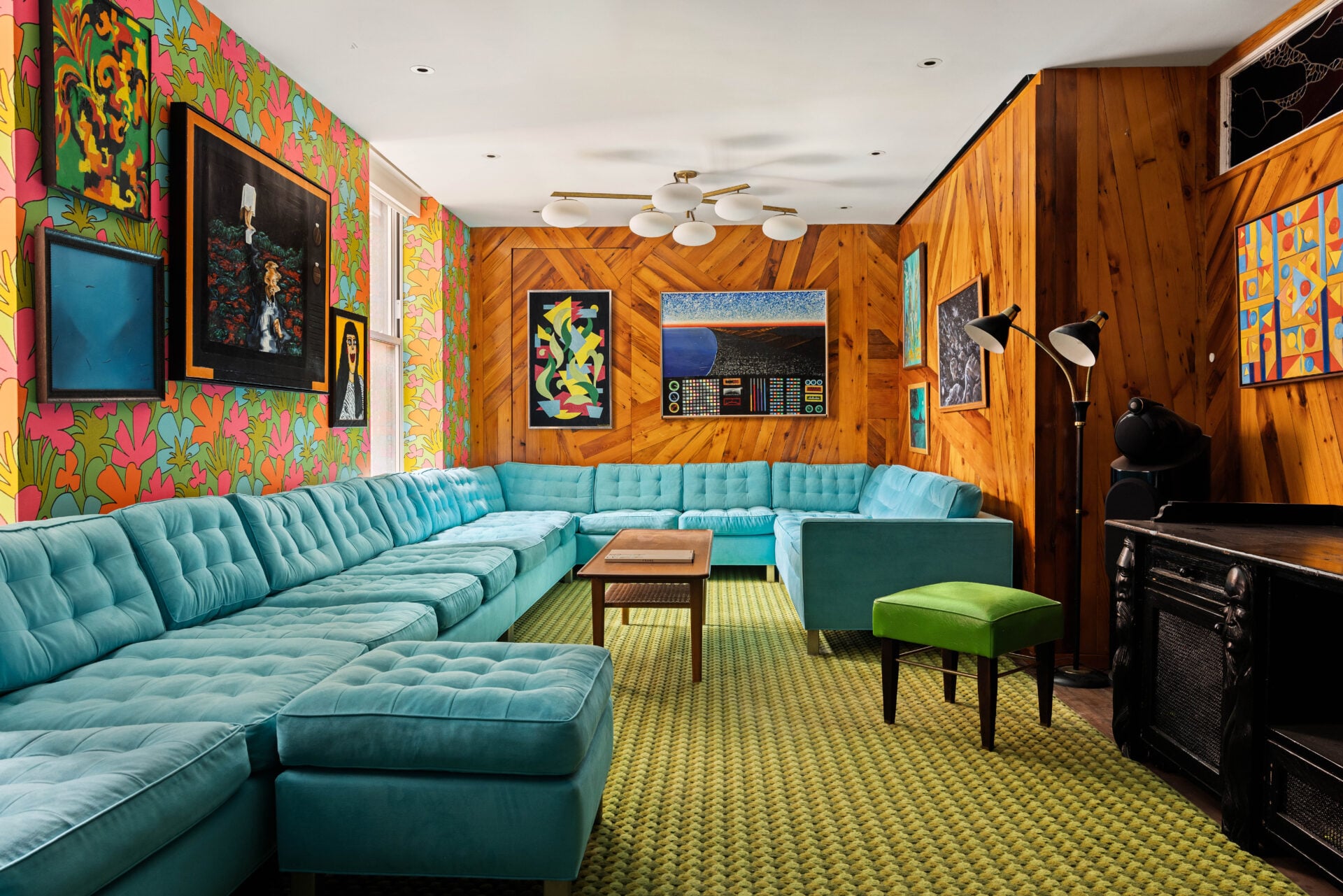 Walking into the seventh-floor living room, walls wrapped in bold vintage-inspired floral wallpaper meet custom wood paneling laid in geometric patterns, creating a layered backdrop for an eclectic collection of artwork.