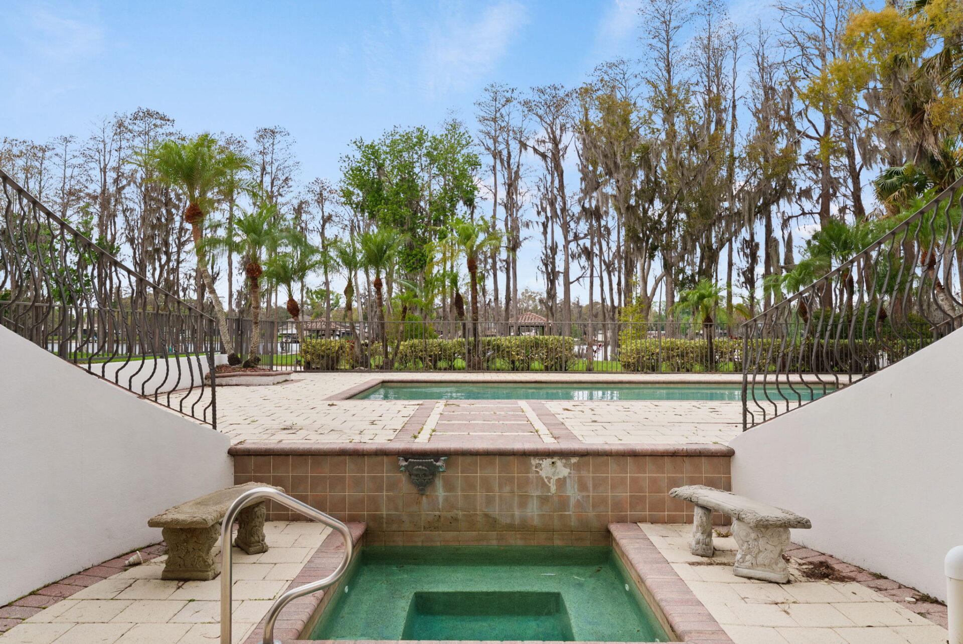 Twin staircases frame a raised spa that overlooks a large rectangular swimming pool surrounded by an expansive paver deck.