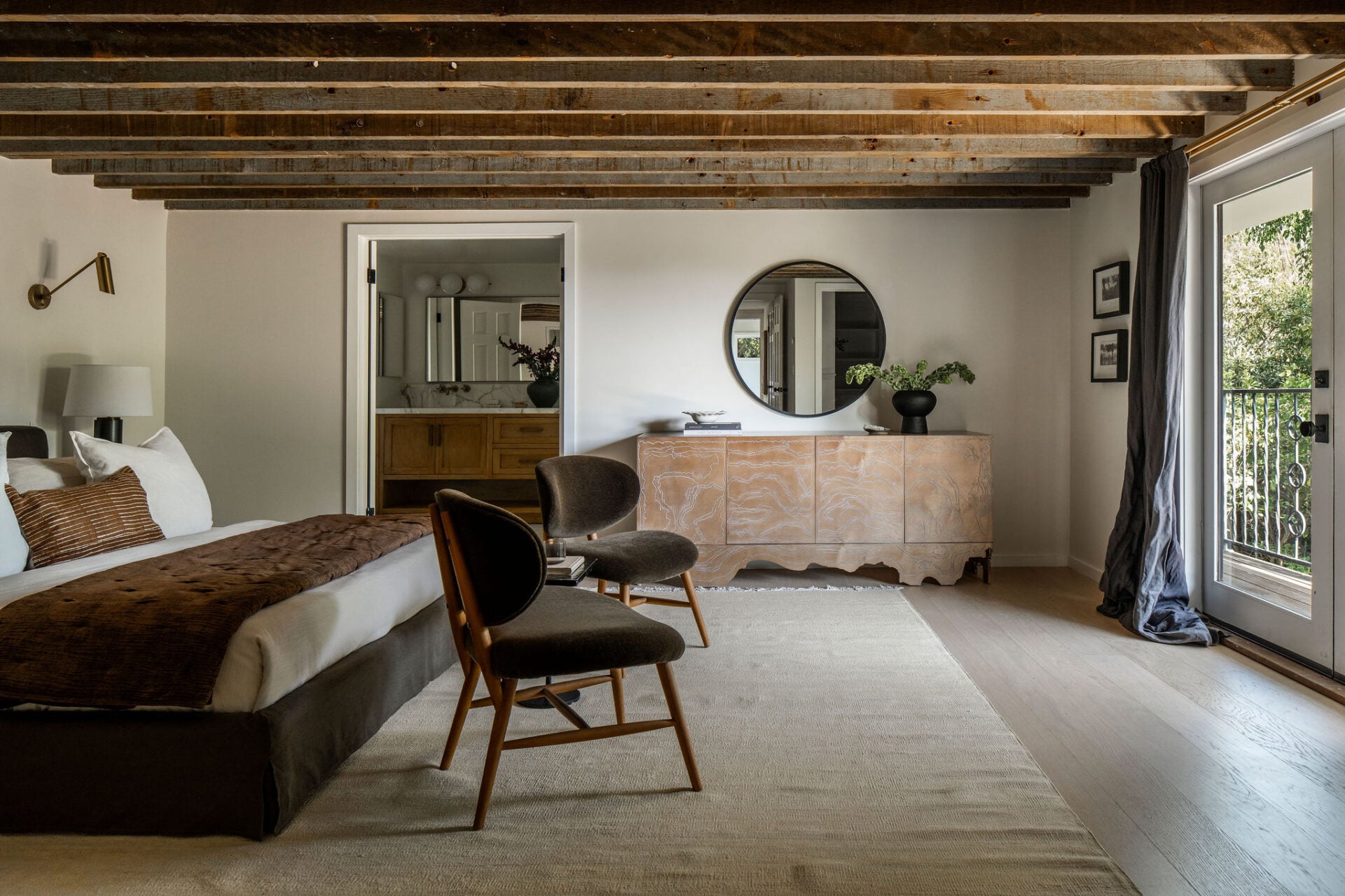 Exposed wood ceiling beams, warm neutral finishes, and direct access to a private deck create a unique connection between the interior and the landscaped grounds.