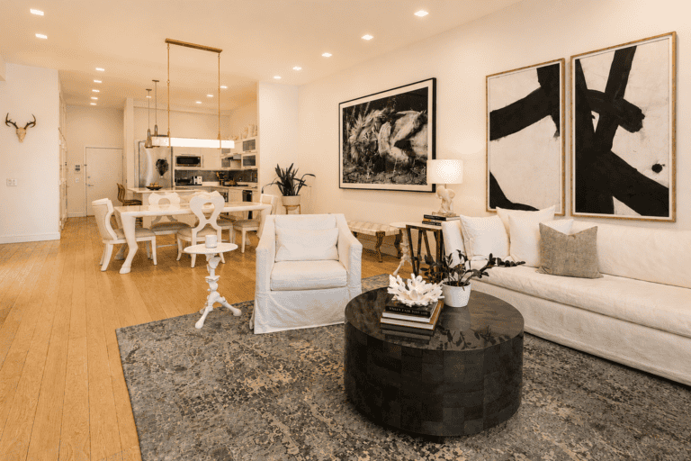 Elegant modern living room with white furniture and abstract art, open-concept kitchen, cozy decor.