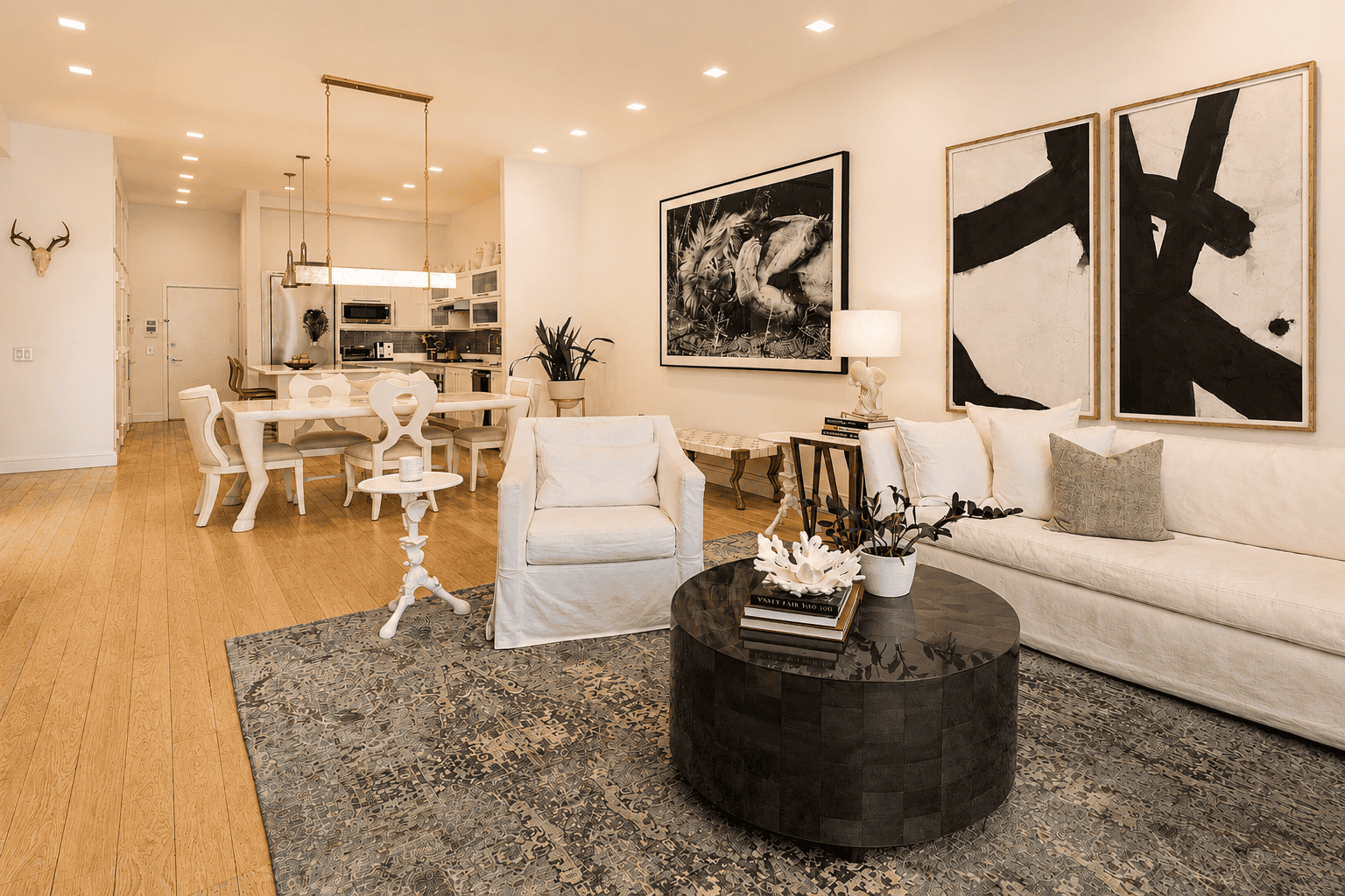 Elegant modern living room with white furniture and abstract art, open-concept kitchen, cozy decor.