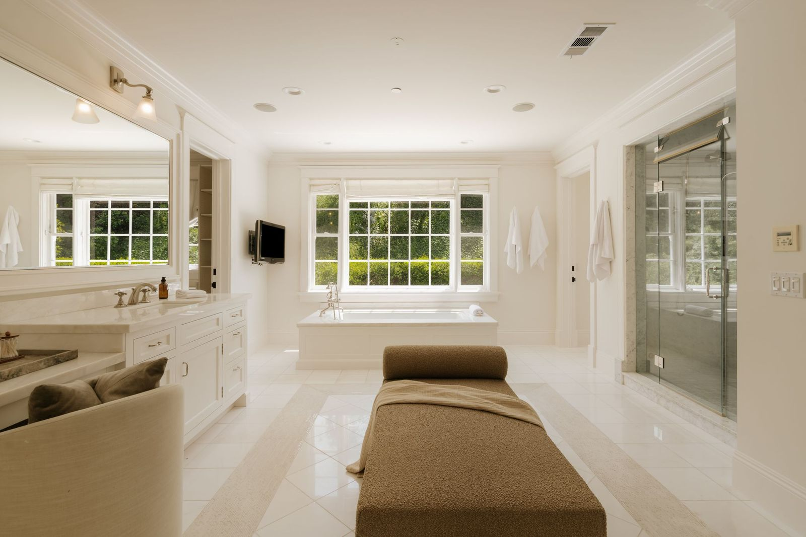 A soaking tub sits beneath a large picture window, while a glass-enclosed shower occupies its own dedicated space within the clean, airy space.