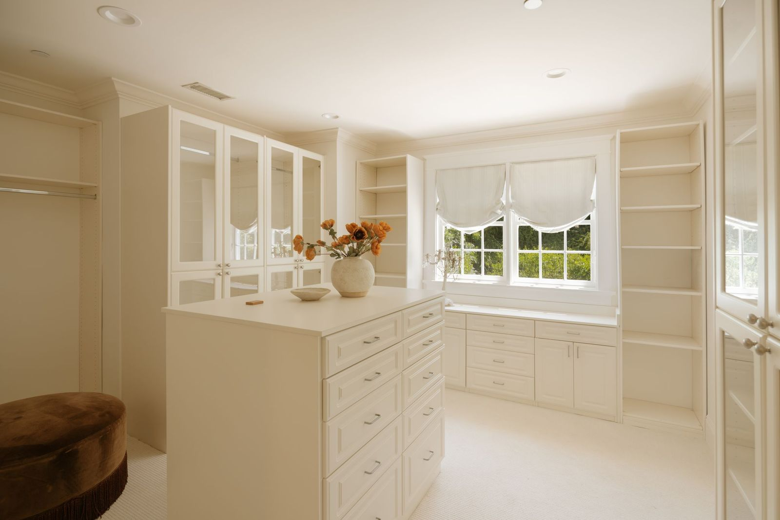 Completing the suite is a substantial walk-in closet outfitted with custom cabinetry, glass-front storage, built-in shelving, and a central island for organization.