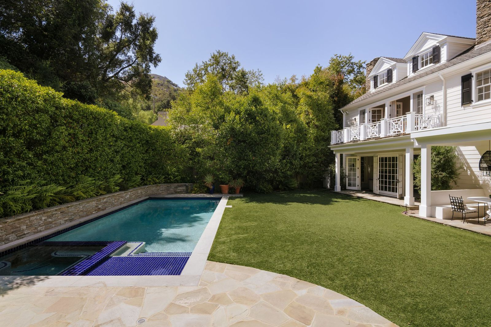 At the center a broad stretch of lawnsits next to a rectangular pool paired with an elevated spa finished in vibrant blue tile.