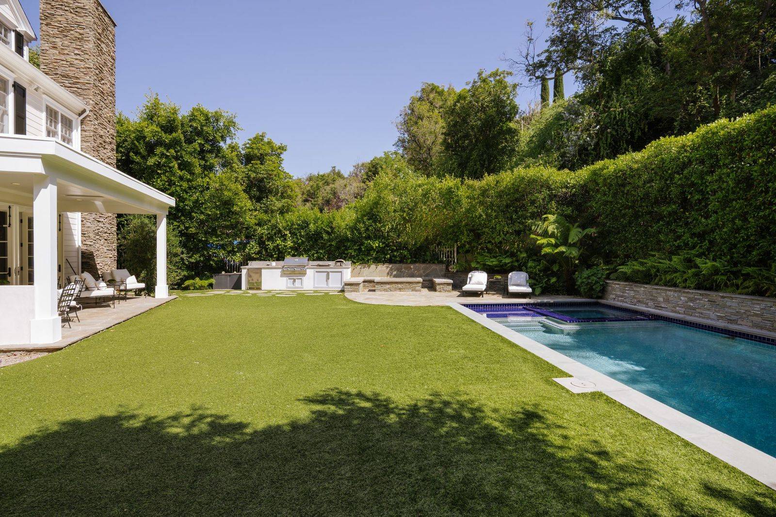 At one end of the pool, an outdoor barbecue station serves as a natural hub for entertaining, accompanied by additional seating areas  beneath covered patios.