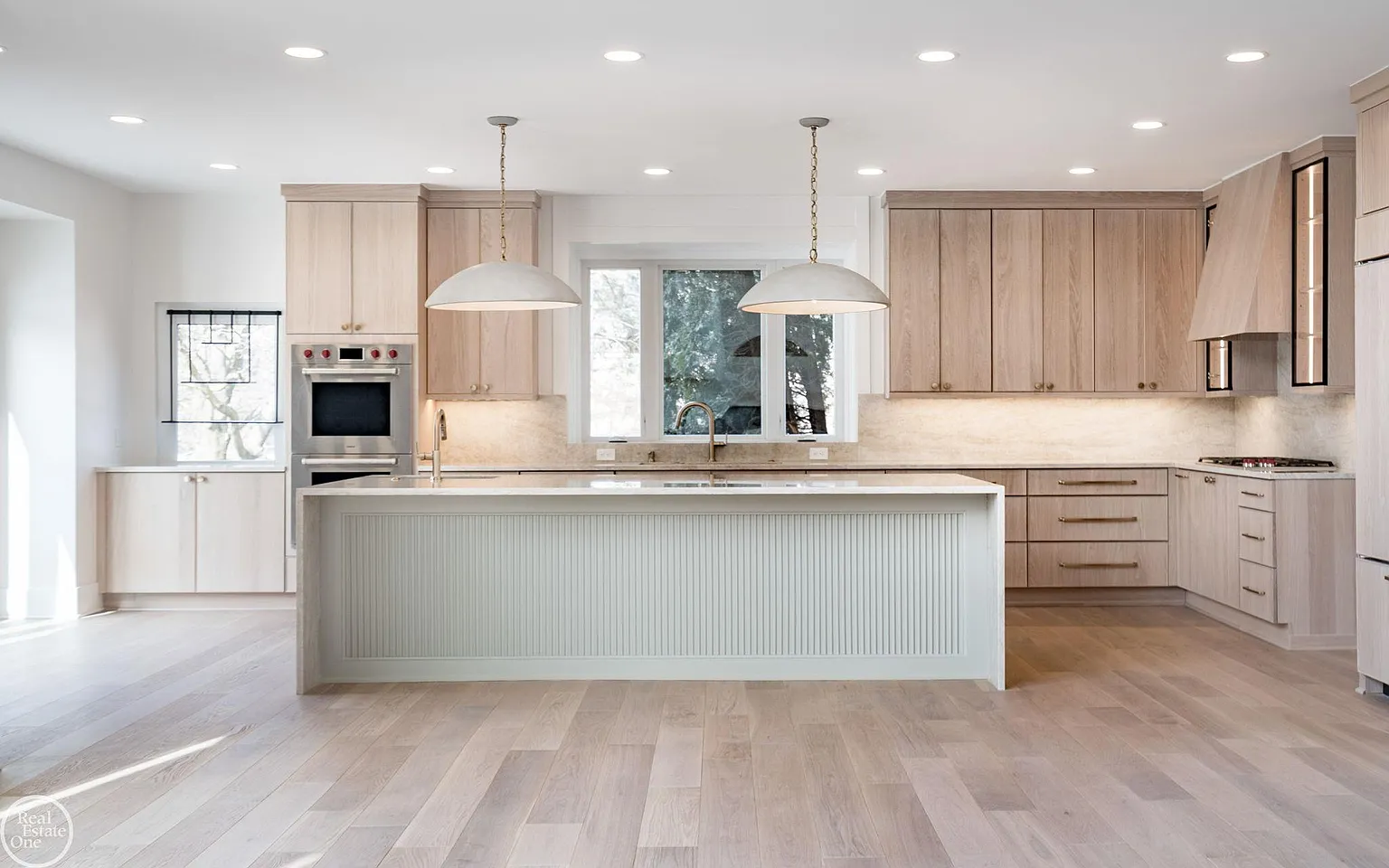 Light wood cabinetry stretches from floor to ceiling, while oversized pendant lights and integrated storage keep the space both functional and visually streamlined.